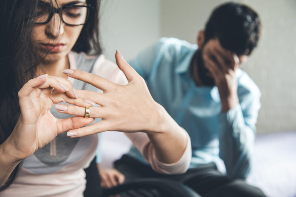 An image of a visibly upset woman taking off wedding ring, with a distraught man in the background, illustrating the painful reality behind the phrase 'God hates divorce'. Their expressions convey the emotional turmoil associated with the dissolution of a marriage.