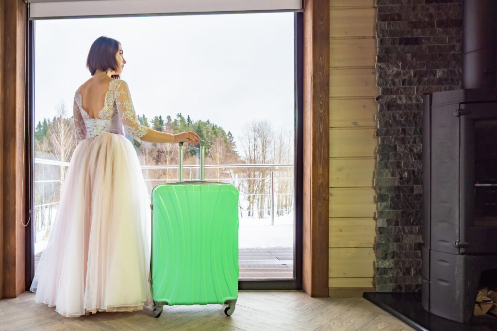 An image of a woman in a wedding dress, standing by the window with a suitcase, symbolizing the tradition of 'leaving parents after marriage'. She looks out, waiting for her groom, conveying the anticipation and bittersweet emotions of starting a new chapter in her life.