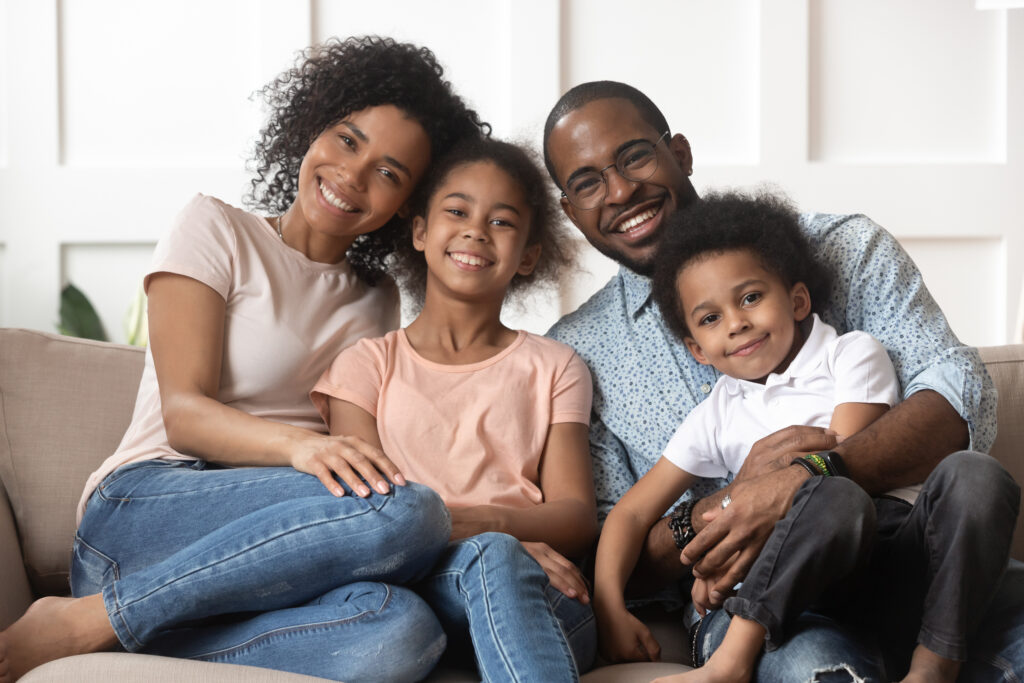 A heartwarming family portrait of a joyful African American family with young children, embodying the sentiment that 'children are a blessing from God'. The image shows relaxed parents sitting on the couch, hugging their preschooler kids, all smiling and posing together, creating an atmosphere of familial love and unity at home.