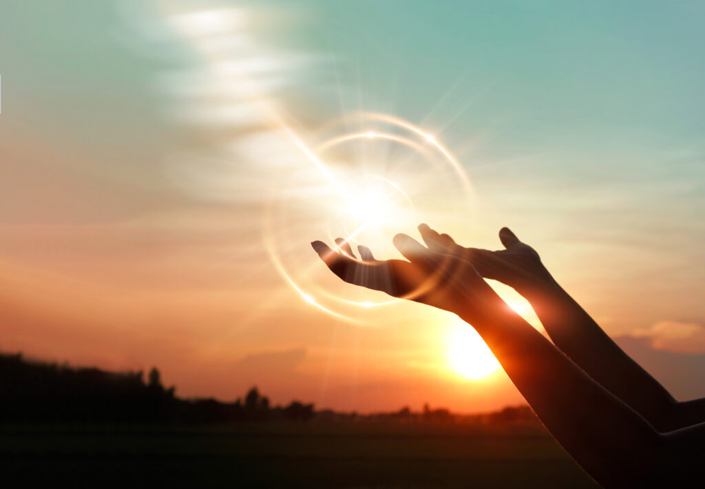 A woman's hands open in prayer seeking divine guidance, illuminated by the warm glow of the setting sun, reflecting upon the Lord's Prayer words.